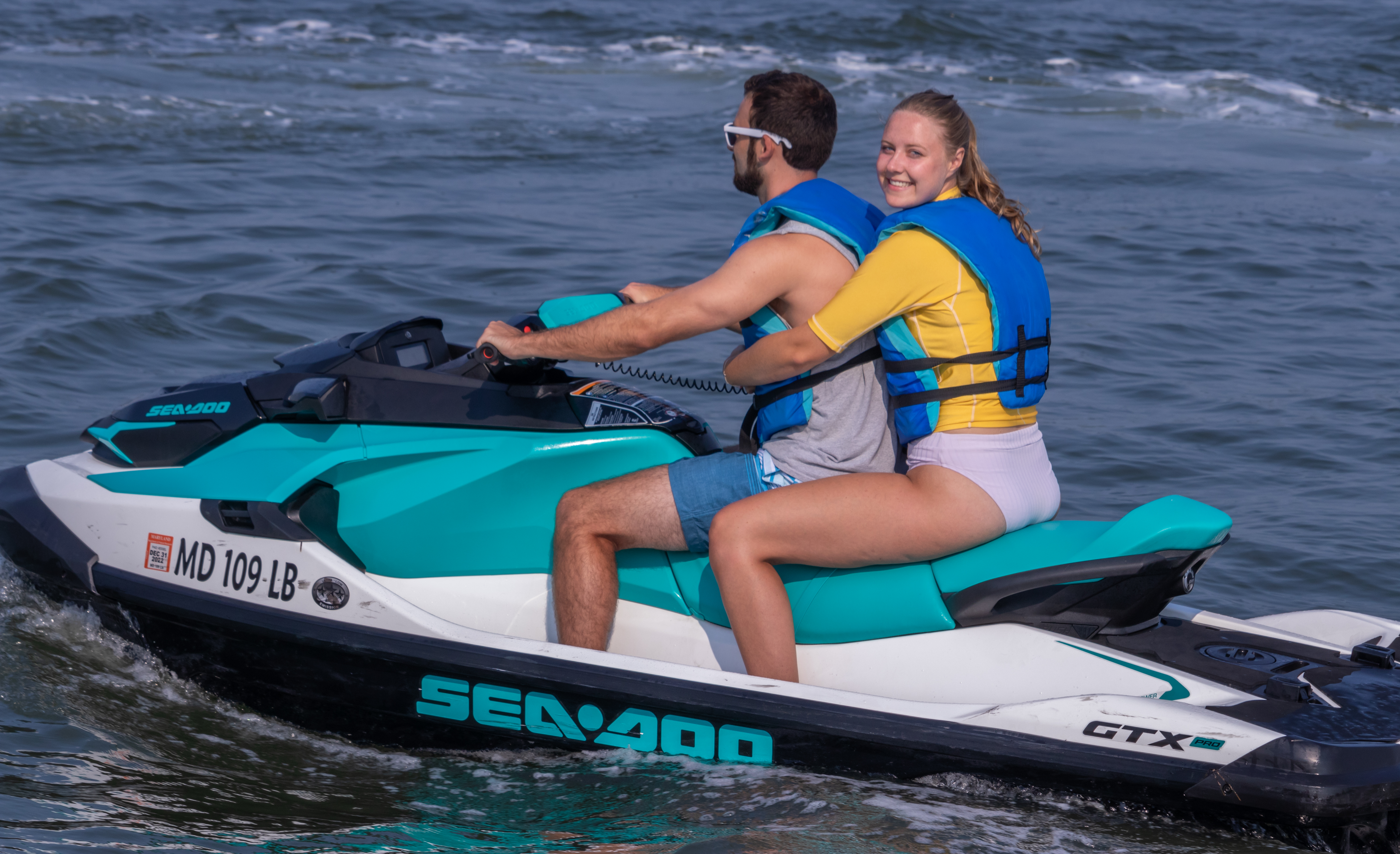 two people wearing blue lifejackets riding one teal jet ski